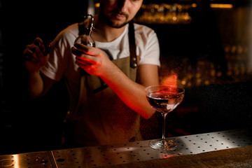 Professional bartender spraying on the cocktail in the glass with a bitter