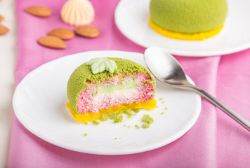 Green mousse cake with pistachio and strawberry cream on a pink textile background. side view, selective focus.