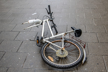 The damaged bicycle lying on the street in the city center. The demolished bicycle on a pavement.