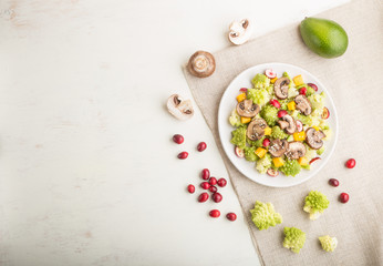 Vegetarian salad from romanesco cabbage, champignons, cranberry, avocado and pumpkin on a white wooden background. top view, copy space.