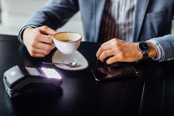 Online payment concept. Man using credit card with mobile phone and coffee cup on restaurant.