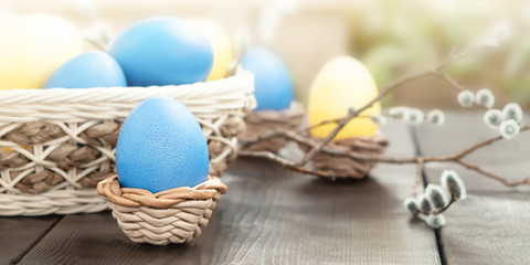 Easter composition - several colored eggs in a basket and on a dark wooden table with willow twigs