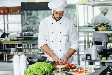 Chief cooking, standing by the stove in the kitchen, cook and smelling the nice aromas from his meal in a pot.
