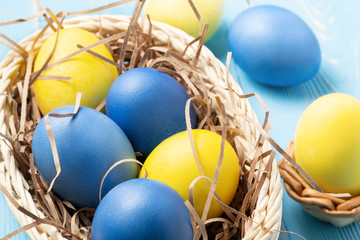 Fototapeta na wymiar Easter composition - several colored eggs in a basket on a blue wooden table