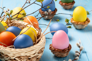 Easter composition - several colored eggs in a basket on a blue wooden table with willow twigs