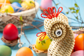 Easter composition - a wicker basket in the form of a chicken with colored eggs on a blue wooden table with willow twigs