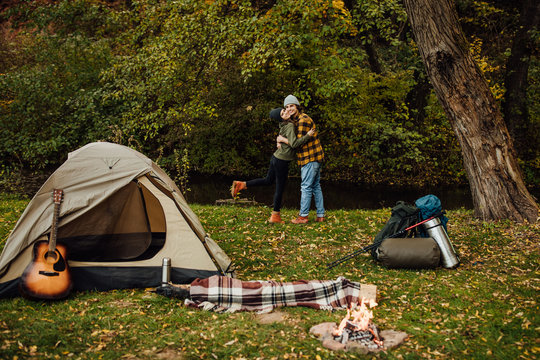 Young beautiful couple hugging in the camp. Attractive woman and handsome man relaxing together in nature near tent.