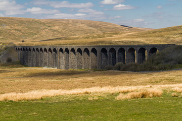 Railway viaduct on sunny day, rolling green hills behind.