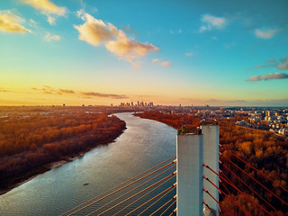 Beautiful panoramic aerial drone view to cable-stayed Siekierkowski Bridge over the Vistula river and Warsaw City skyscrapers, Poland in gold red autumn colors in November evening at sunset