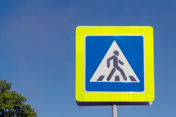Pedestrian crossing road sign against a blue sky.