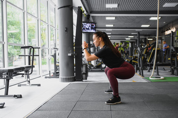 Fototapeta na wymiar Side view portrait of a young woman doing squats at fitness gym