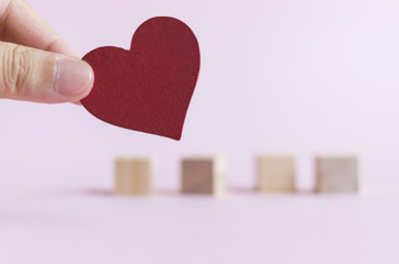 Closeup men hand holds red heart shape wooden piece with blur wooden cubes as back ground
