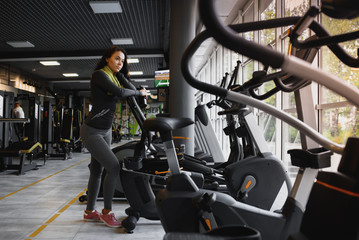 Fototapeta premium Young woman drinking water and taking a break after workout in gym,