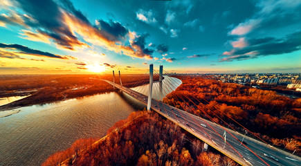 Beautiful panoramic aerial drone view to cable-stayed Siekierkowski Bridge over the Vistula river and Warsaw City skyscrapers, Poland in gold red autumn colors in November evening at sunset - obrazy, fototapety, plakaty