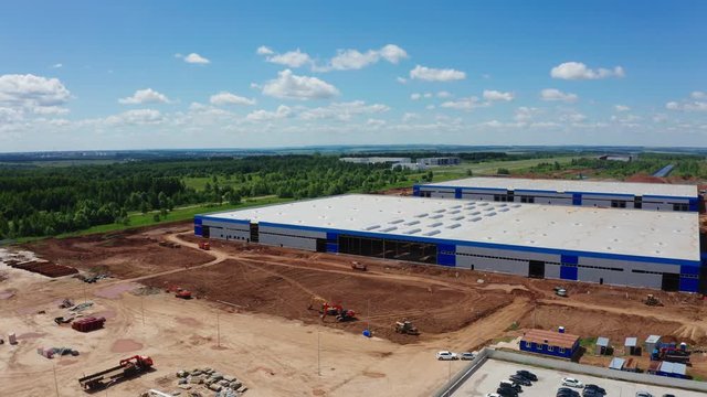 cars drive along new warehouse on construction site aerial