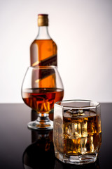 Whiskey with ice on a dark background. In the background a glass of whiskey and a full bottle of whiskey