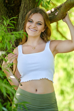 Stunning young female fashion model poses in park near willow tree Ð summer smiling..