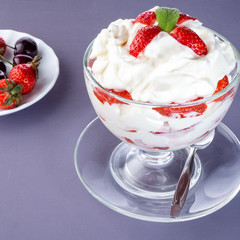 Strawberries with whipped cream in a glass bowl and berries in the background - 306792779