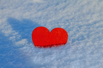 wooden red heart lies half in white snow on a sunny day