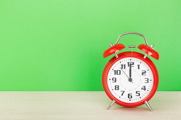 Red retro alarm clock with twelve o'clock, on wooden table on a green background. The concept of time, holiday, event start, deadline. Layout with copy space for your text.