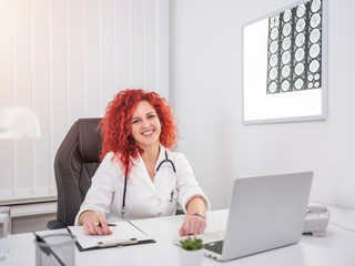 Smiling medical worker sitting in white coat with stethoscope around her neck.