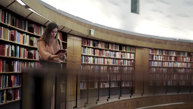 Nice girl holds a book in her hands and reads in the library. Learning something new.