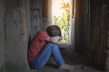 Young girl in despair sitting alone in old brick room. poor homeless concept