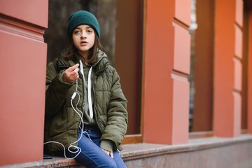 young stylish beautiful teen girl listening to music, mobile phone, headphones, enjoying, denim outfit, smiling, happy, cool accessories, having fun, laughing, park