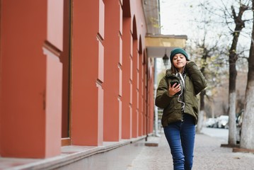 Obraz na płótnie Canvas young stylish beautiful teen girl listening to music, mobile phone, headphones, enjoying, denim outfit, smiling, happy, cool accessories, having fun, laughing, park