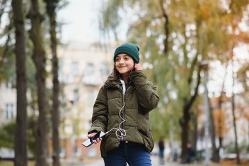 young stylish beautiful teen girl listening to music, mobile phone, headphones, enjoying, denim outfit, smiling, happy, cool accessories, having fun, laughing, park