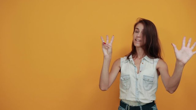 Crazy caucasian young woman in blue denim shirt showing nine fingers isolated on orange background in studio. People sincere emotions, lifestyle concept.