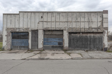 Front of a long abandoned storefront with garage door, boarded up windows and broken glass