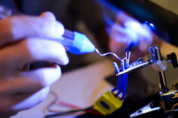 Smoke appears while soldering ESC and rotor wires with helper hands. Technology and electrical engineering concept. Autonomous vehicles like drones need a lot of soldering in building process