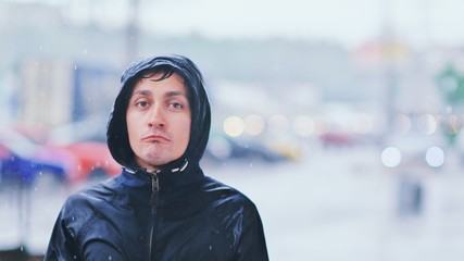 Portrait of a sad man in a raincoat and a hood in the rain. Bad stormy rainy weather concept.