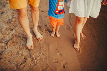 Happy family on the beach. Closeup of family feet with boy baby walking on sand. Man and woman holding their baby. Walk by the river. Travel lifestyle, parents with kids on summer vacation