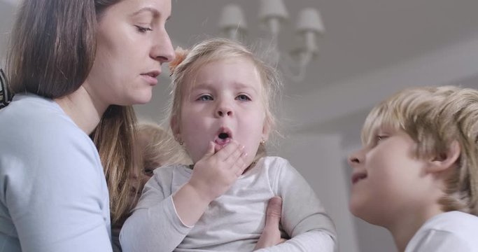 Close-up portrait of crying Caucasian baby girl. Mother kissing her lovely daughetr on cheek, worried brother talking to sister. Family taking care of each other. Cinema 4k ProRes HQ.