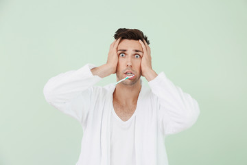 Shocked man in bathrobe cleaning teeth on color background