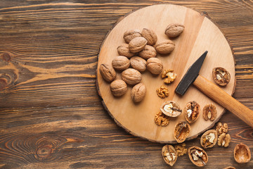 Fototapeta na wymiar Board with tasty walnuts and hammer on wooden table