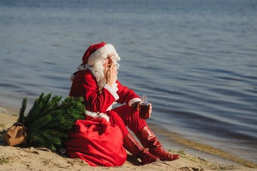Obraz premium Authentic Santa Claus with bottle of drink relaxing on beach
