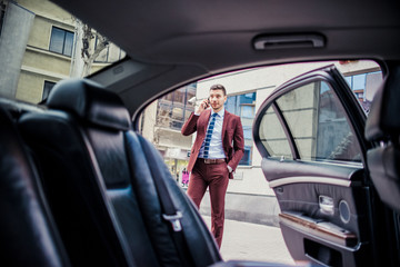 Man in suit speaking on mobile near the luxury car