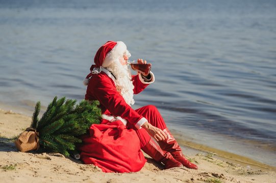 Santa Claus on the beach drinks whiskey and smokes a cigar.