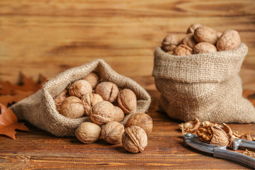 Sacks with tasty walnuts and nutcracker on wooden table