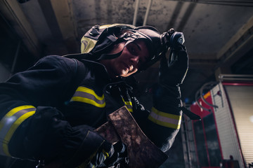 Fototapeta na wymiar Portrait of a female firefighter while holding an axe and wearing an oxygen mask indoors surrounded by smoke.