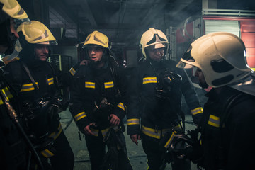 Team of firefighters standing inside ( indoors ) a buliding next to a fire engine.