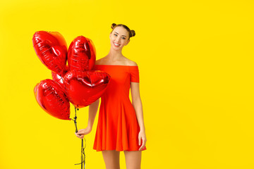 Beautiful young woman with heart-shaped balloons on color background
