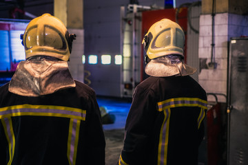 Two young men wearing helmets posing from the back inside the fire station.