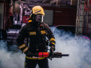 Obraz premium Portrait of young fireman standing and holding a chainsaw in the middle of the chainsaw's smoke .
