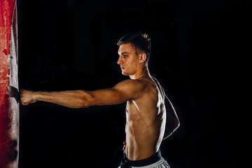 Karate shirtless sportsman hitting punching bag isolated on black