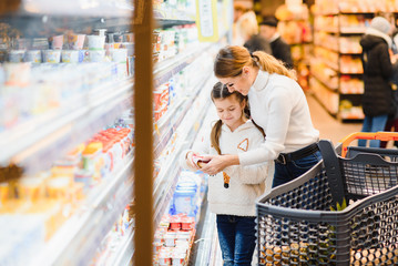 Family in the supermarket. Beautiful young mom and her little daughter smiling and buying food. The concept of healthy eating. Harvest