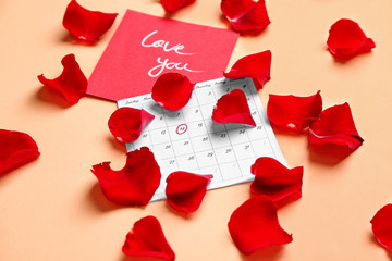 Calendar with marked date of Valentine's Day, card and rose petals on color background